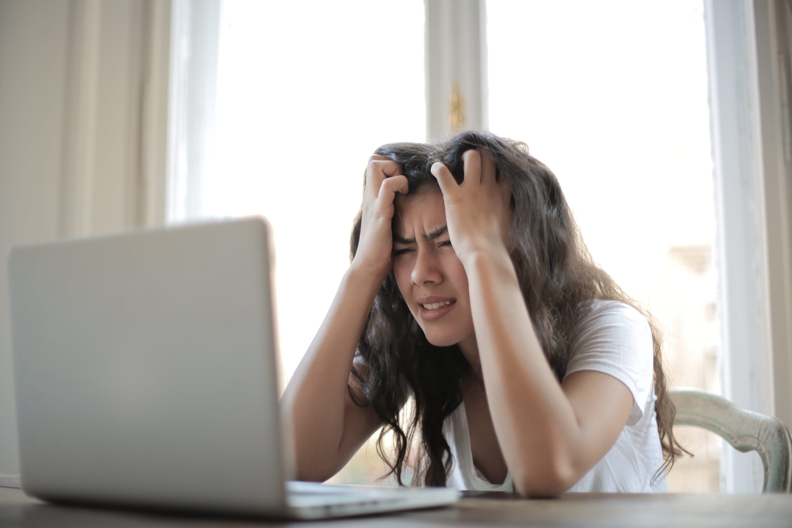 A frustrated woman running her hands through her hair while looking at a laptop | Source: Pexels